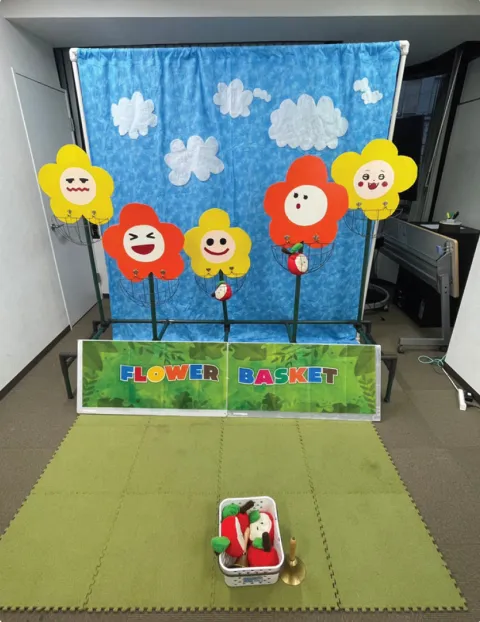 空の絵の背景布に花の的が並び、手前にカゴが置いてある