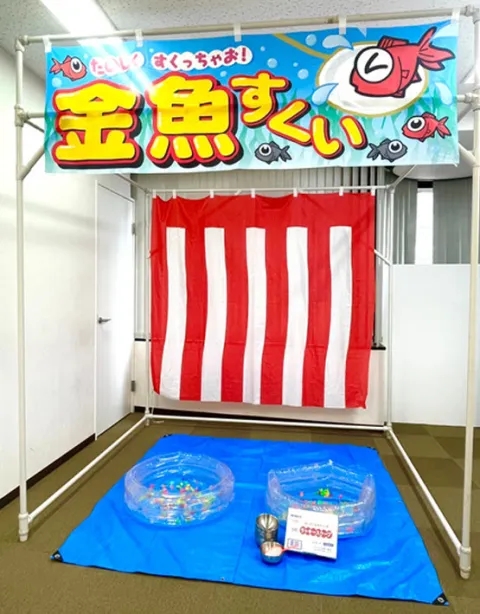 金魚すくいの屋台。紅白幕の前のシートに、ビニールプールとおわんが置いてある