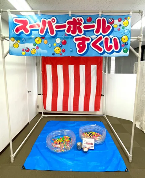 スーパーボールすくいの屋台。紅白幕の前に、スーパーボールの入ったプールがある